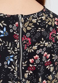 Tissu noir avec un motif floral comprenant des fleurs bleues, rouges et crème. Comprend une fermeture éclair en métal argenté au dos.