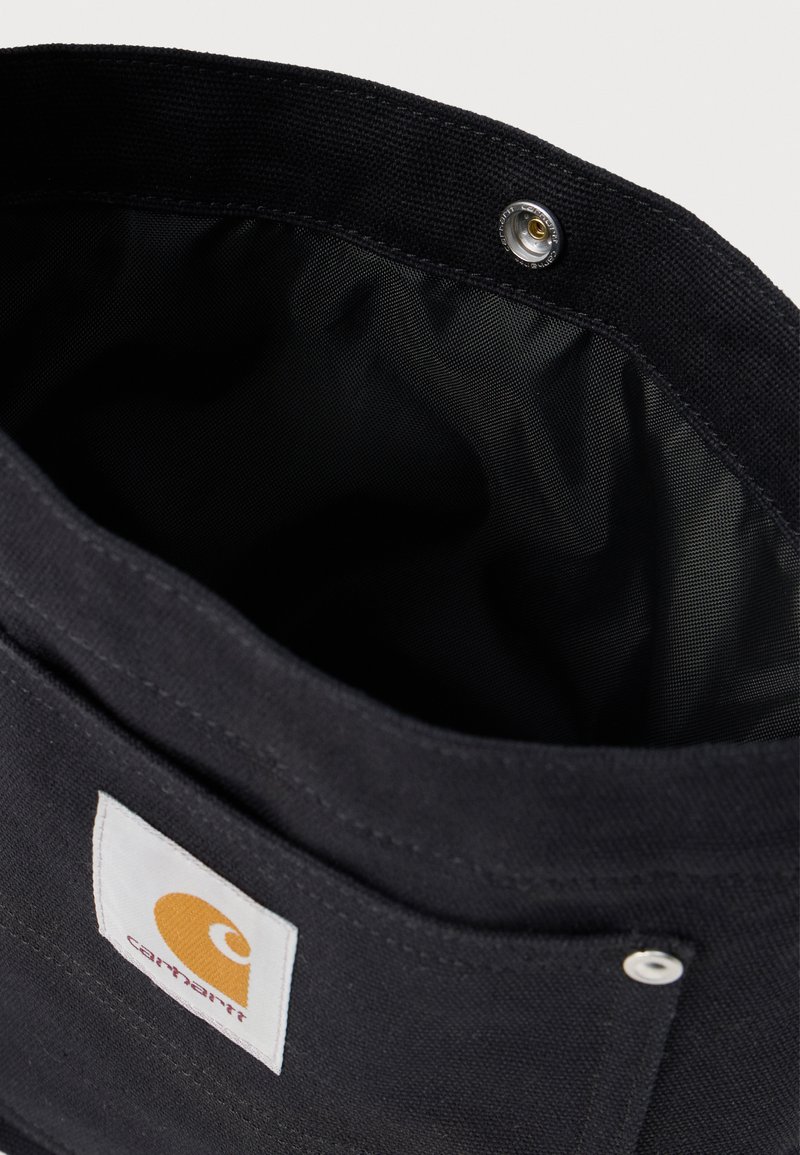 Black Carhartt fabric bag with white rectangular logo patch, snap button closure, and visible textured interior lining.