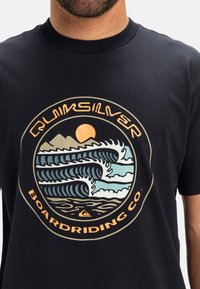 Black t-shirt featuring a circular graphic with waves, mountains, and sun in colors of blue, cream, and orange. Short sleeves and crew neck design.
