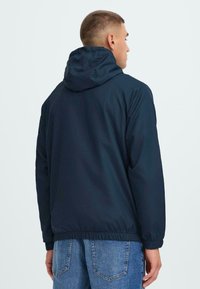 Navy hooded jacket with elastic cuffs and hem, featuring a lightweight material and clean design. No visible logos or embellishments.