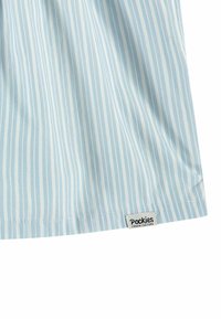 Tissu rayé bleu clair avec des rayures alternées fines et larges. Les étiquettes indiquent "Pockies" et "Couch Culture" près de l'ourlet inférieur.