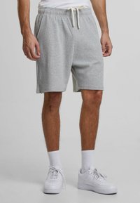 Shorts griși din bumbac, cu talie elastică și șnur, dotate cu buzunare laterale și o croială lejeră, asortate cu teniși albi.