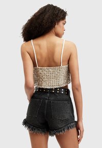 Top chiaro tagliato con un motivo testurizzato, abbinato a pantaloni shorts in denim neri con orli sfrangiati e una cintura con borchie.