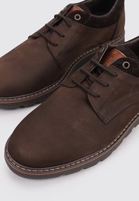 Zapatos de cuero marrón con un acabado suave, diseño con cordones, punta redondeada, costura contrastante y suela de goma. Presentan una pequeña etiqueta de marca.