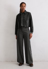 Czarna skórzana kurtka do pasa, szary dopasowany top oraz szare szerokie spodnie o teksturowanym wykończeniu. Brązowe buty z okrągłym czubkiem.