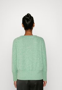 Ljusgrön tröja med struktureradstickning, bred rund hals, och ribbade muddar och nederkant. Har sänkt axlar för en avslappnad passform.