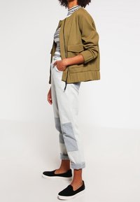 Olivgrön bomberjacka med sänkta axlar, tillsammans med randig polotröja, ljusblå denimbyxor och svarta slip-on skor.