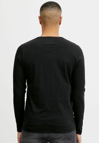 Black long-sleeve shirt with a round neckline, made of soft fabric, featuring a fitted design and minimal stitching details on the back.