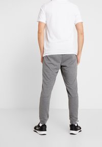 Šedé tepláky s elastickými manžetami, doplněné obyčejným bílým tričkem. Černé sportovní boty outfit doplňují. Jednoduchý design, bez vzorů.