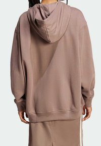 Överstor brun hoodie i mjukt material, med justerbar huva, ribbade muddar och en avslappnad silhuett. Minimalistisk design.