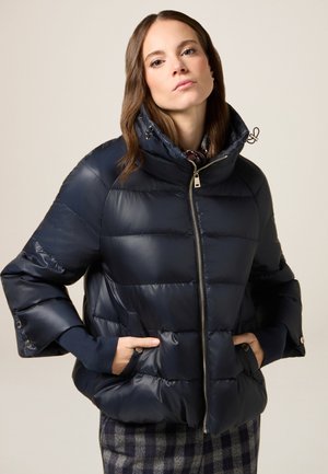 Granatowa kurtka puchowa wykonana z błyszczącego materiału, z wysokim kołnierzem, zamkiem błyskawicznym z przodu i kieszeniami bocznymi. Żebrowane mankiety dopełniają projekt.