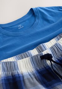 T-shirt bleu à col rond associé à un pantalon de pyjama à carreaux bleu et blanc avec cordon, posé à plat sur une surface blanche.