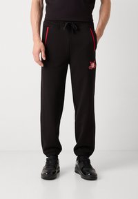 Zwarte sweatpants met een elastische tailleband en boorden, featuring rode accenten op de zakken en een rode geborduurde ontwerp op het voorbeen.