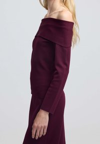 Bordowa bluzka typu off-the-shoulder z długimi rękawami, dopasowany krój, gładka tekstura i szeroki dekolt, w połączeniu z pasującymi spodniami.