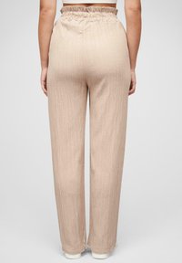 Pantalons larges beige clair en tissu texturé, avec une taille élastique froncée et une finition lisse.