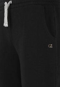 Zwarte joggingbroek met een elastische tailleband, een grijs trekkoord, zijzakken, en een klein geborduurd logo op de dij. Zacht katoenen stof.