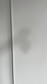 Parete grigia con una texture liscia e una leggera ombra che forma una forma circolare vicino al bordo, incorniciata da una sottile finitura chiara.