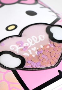 Hello Kitty-Notizbuch mit pinkem und schwarzem Cover, das ein herzförmiges Fenster mit pinken und lila Konfetti-Herzen enthält.