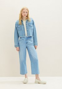 Helles blaues Jeansjacke mit einem cropped Design, kombiniert mit hoch taillierten hellblauen weit geschnittenen Jeans und beigen Slip-On-Schuhen.
