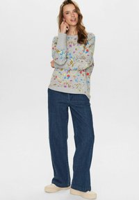 Svetlo šedý sweatshirt s mnohými farebnými kvetinovými vzormi; kombinovaný s tmavomodrými širokými nohavicami a béžovými platformovými teniskami.