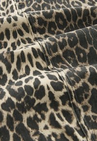 Nahaufnahme von beigem Stoff mit schwarzem und braunem Leopardenmuster sowie sichtbaren genähten Nähten.