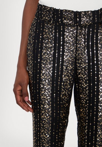 Black and gold sequin pants with vertical stripes, featuring a stretchy waistband and a smooth texture. Hand partially visible.