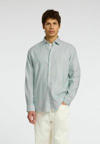 Camicia verde chiaro a maniche lunghe con colletto all'americana, bottoni bianchi e una vestibilità comoda, abbinata a pantaloni color crema.