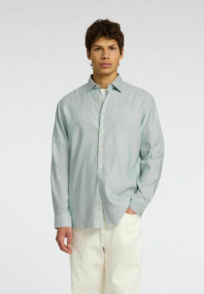 Camicia verde chiaro a maniche lunghe con colletto all'americana, bottoni bianchi e una vestibilità comoda, abbinata a pantaloni color crema.