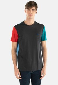 Kortærmet t-shirt med sort krop, røde og teal ærmer og et lille blåt logo på brystet. Lavet af bomuldsstof, afslappet pasform.