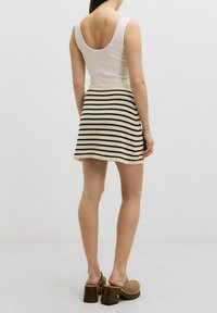 Weißes Tanktop mit ausgeschnittenem Rücken; gestreifte beige und schwarze Röcke; braune Plateauschuhe mit Nietenakzenten; glatte Textur und lässiger Schnitt.