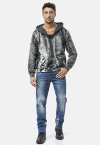 Zwart-grijs patroon zip-up hoodie met een capuchon en trekkoord, gecombineerd met vervaagde blauwe spijkerbroeken en zwarte veterlaarzen.