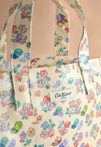 Borsa a tracolla floreale con sfondo crema, caratterizzata da fiori e foglie colorate. Tessuto resistente con manici cuciti e toppa con logo.