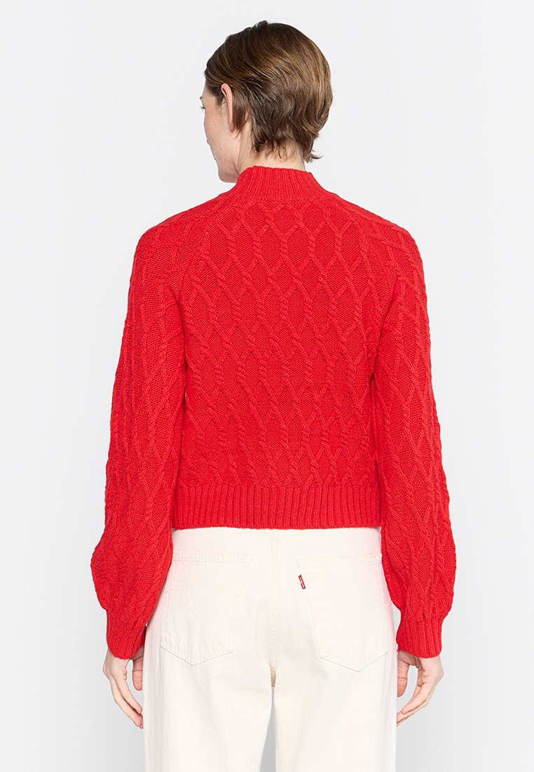 Maglione rosso lavorato a maglia con un motivo a diamante testurizzato, scollatura rotonda e orlo a costine. Maniche lunghe e leggermente arricciate arricchiscono il design.