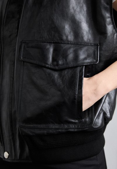 Zwarte leren gilet met een gladde textuur, voorzien van een voorzak, geribde zwarte gebreide zoom en zilveren drukknoopsluiting.