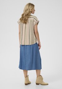 Top corto multicolore a maniche corte con motivi verticali in rosa e verde, abbinato a una gonna midi in denim e stivaletti beige alla caviglia.