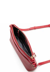Borsa a tracolla rossa in pelle con finitura texturizzata, scomparto principale con zip e tracolla regolabile. L'interno presenta una fodera nera e tasche.