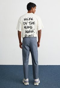 Cream t-shirt with large black text on the back, paired with grey trousers. The pants feature a back pocket and are tapered. White sneakers.