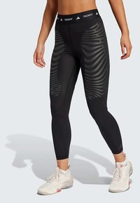 Sorte leggings med høy midje som har et teksturert, rillestrukturert mønster langs sidene, laget av et elastisk, pustende materiale.