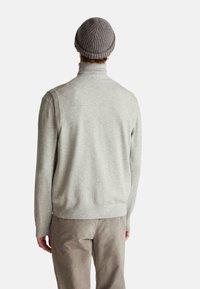 Maglione grigio a maglia con colletto alto, texture liscia e dettagli a coste, abbinato a pantaloni in velluto a coste grigi e un berretto abbinato.