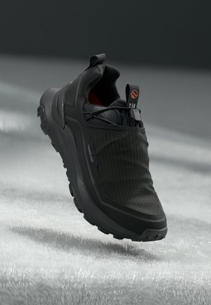 Czarny sneaker Timberland z fakturowaną podeszwą i pętelkami do ściągania, ustawiony na miękkiej, jasnej powierzchni z zacienionym tłem.