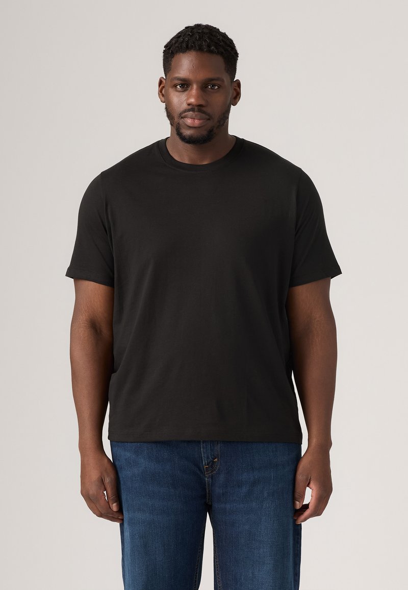 T-shirt en coton noir avec un col rond et des manches courtes. Le t-shirt a une coupe décontractée, associé à un jean en denim bleu.