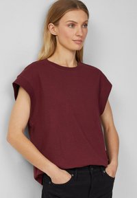 Burgunderfarbenes Kurzarm-T-Shirt aus Baumwolle, mit lockerer Passform, Rundhalsausschnitt und umgeschlagenen Ärmeln. Tragen Sie es zu schwarzen Hosen.