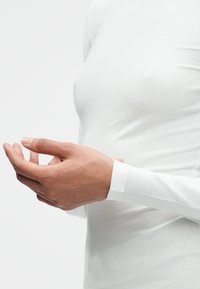 Biała koszula z długim rękawem, dopasowana, wykonana z lekkiej bawełny, o gładkiej fakturze, z ręką umieszczoną w okolicy talii, subtelne detale przeszycia.