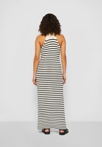 Robe maxi avec un col halter, fabriquée en tissu tricoté avec des rayures horizontales noires et crème alternées, texturée avec une silhouette ajustée.
