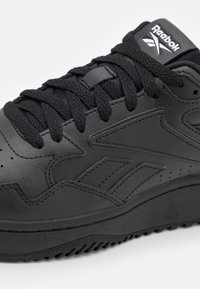 Zwarte leren sneaker met een gestructureerd oppervlak, ronde veters, gevoerde tong en rubberen zool met een trijpatroon. Reebok-logo op de tong.