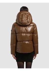 Giacca imbottita marrone con finitura lucida, cappuccio oversize e dettaglio del logo sul cappuccio. Presenta trapuntatura orizzontale e un'etichetta con il logo laterale.