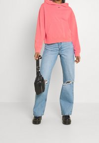 Růžová mikina s kapucí a přední kapsou, kombinovaná se světle modrými, roztrhanými širokými džíny. Doplněno černou crossbody taškou a robustními černými botami.