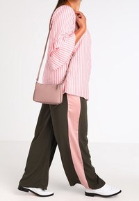 Růžovo-bíle pruhovaná blůza s rozšířenými rukávy, spojená s olivově zelenými kalhotami s růžovým bočním pruhem. Bílé boty a růžová taška.