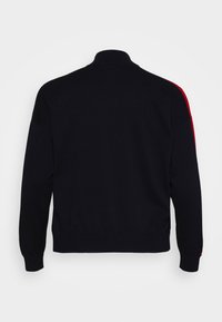 Veste en tricot noire avec un col haut, des rayures rouges le long des épaules, et des poignets et un ourlet côtelés. Texture lisse, design décontracté.