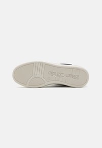 Schuhsohle mit einer glatten beigen GummOberfläche, die über strukturierte Profils und ein geprägtes Logo verfügt. Abgerundeter Fersenbereich mit gerippten Akzenten.